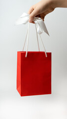 A child's hand holds a gift red bag with a white ribbon on a white background, get a surprise gift. Concepts of birthday, saint valentine. Congratulations women.