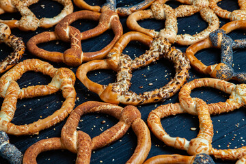Fresh prepared homemade soft pretzels. Different types of baked bagels with seeds on a black background.