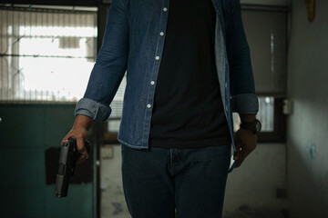 A man in a blue jeans shirt with a mask and a silver cap is standing in the room with a pistol....