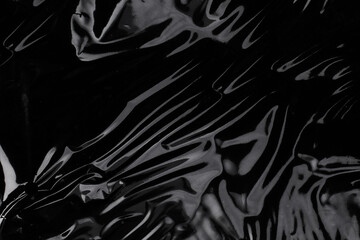 Wrinkled plastic wrap texture on a black background. Cellophane package wallpaper