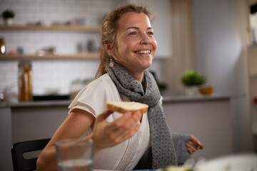 Beautiful businesswoman enjoying in breakfast. Happy young woman eating sandwich at home.