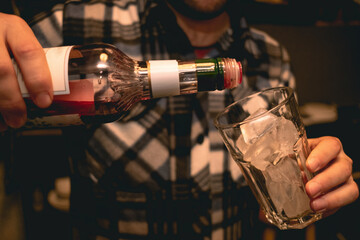 Hands of bartender pouring red liqueur into glass with ice