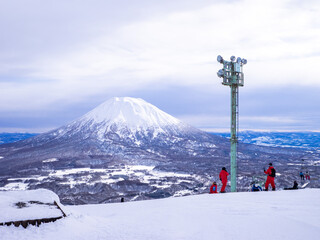Naklejka na ściany i meble Skiers with snowy volcano seen from a ski resort (Niseko, Hokkaido, Japan)
