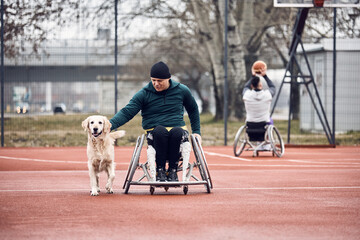 Athletic man in wheelchair enjoys with his dog on basketball court outdoors.