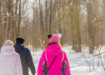 Fototapeta na wymiar A girl in a hat with ears walks through the winter forest with her parents