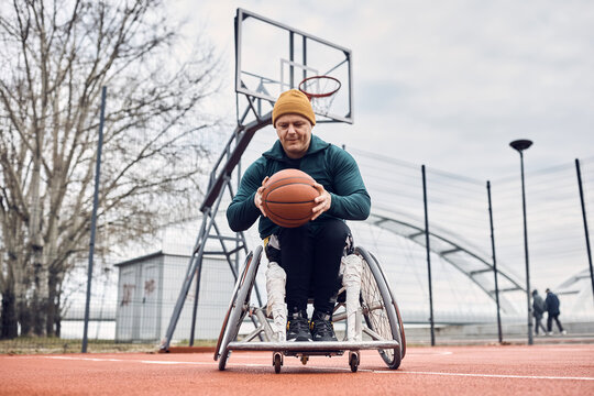 Sportsman with disability exercises wheelchair basketball on outdoor court.