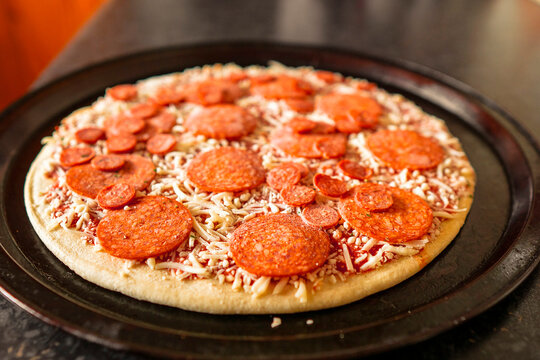 Simple uncooked pepperoni pizza on a metal round cooking tray. Italian world known dish with dough, cheese and meat and sauce.