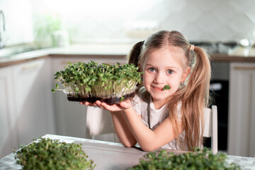 Cheerful girl is eating green salad at home in the kitchen. The concept of healthy food for...