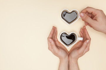 Woman and man hands holds heart shaped cup of coffee.