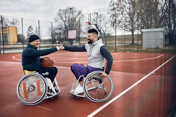 Happy wheelchair basketball players fist bumping while greeting on outdoor court.