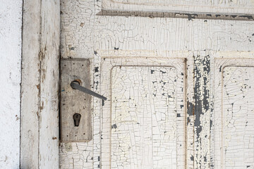 Old front door with cracked texture and damage paint. Close up cracked damaged paint. Old wooden door with metal handle. Retro texture.
