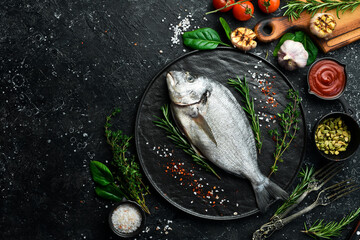 Sea fish dorado with spices are ready to cook. Top view. On a black stone background.
