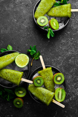 summer popsicles with lime and kiwi. On a black stone background.