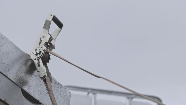 Slow motion of a male worker kneels for secure a tie-down ratchet strap. Hand close up locking up