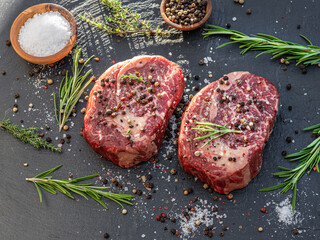Raw Ribeye steaks with salt and herbs on grey board. Top view.