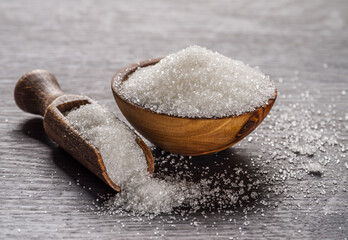 White refined sugar in wooden bowl and spoon on dark wooden table.