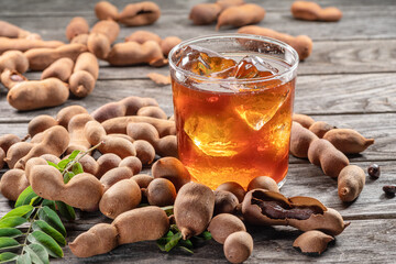 Glass of cool refreshing tamarind drink and some tamarind fruit on wooden table.