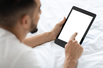 Arab Man Using Digital Tablet With Blank Screen While Lying In Bed