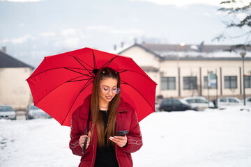young girl with a red umbrella looks at her mobile phone