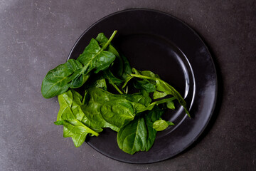 fresh green spinach leaves on dark black table in black dish top view. concept of vegan healthy food