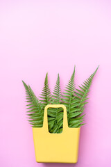 fern leaves in a yellow basket on a pink background, top view, flat lay