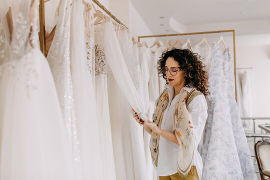 Woman Choosing Wedding Dress In A Showroom. Future Bride Buying A Wedding Gown In A Shop.