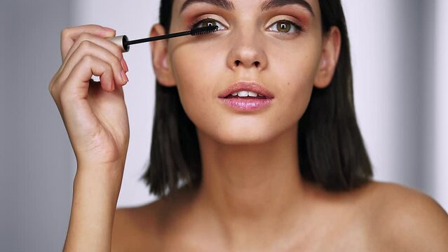 Woman applies black mascara on her eyelashes, finishing her makeup. Beauty concept. Close up