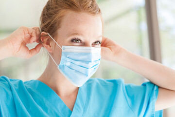 Beautiful young redhead woman nurse in scrubs wearing medical pandemic face mask covering
