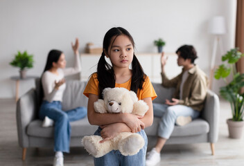Lonely sad chinese teen girl with toy suffers from scandal of parents, young asian lady and guy quarreling at home