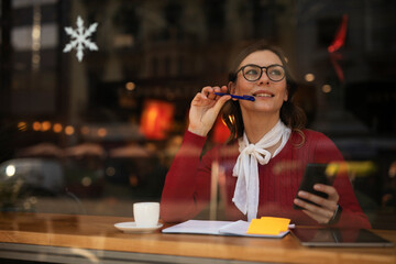Stylish young woman drinking coffee at cafe. Beautiful girl using the phone while enjoy in fresh coffee