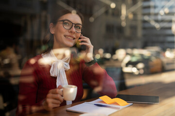 Stylish young woman drinking coffee at cafe. Beautiful girl talking to the phone while enjoy in fresh coffee