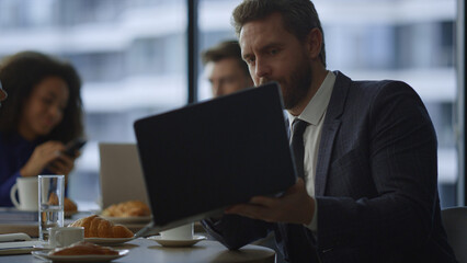 Busy manager showing laptop computer to business colleague in restaurant cafe.