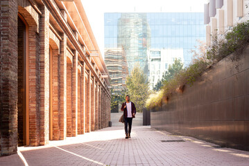 Front view of a attractive young man holding shoulder bag walking through the city