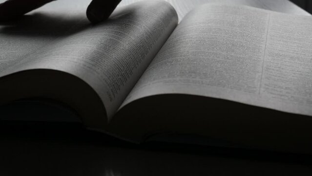 A woman's hand turns the pages of a book or dictionary in the dark, close-up