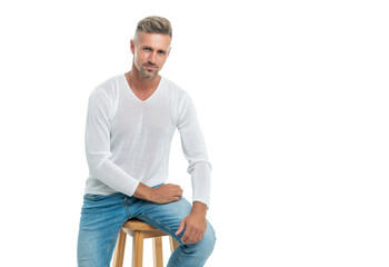 smiling handsome mature guy with graying hair sit on chair isolated on white, mens beauty.