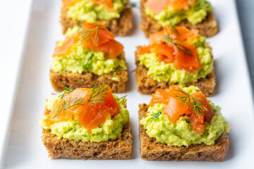 Toasts with avocado and smoked salmon on the wooden plate