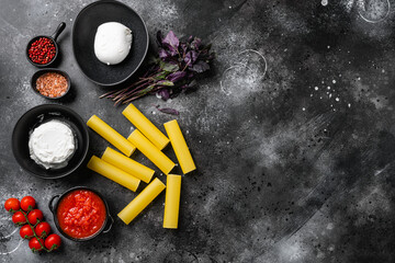Cannelloni with ingredients, on black dark stone table background, top view flat lay, with copy space for text