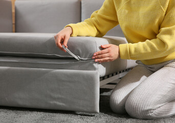 Young woman unfolding sofa into a bed in room, closeup. Modern interior