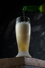 Beer pouring into cup in a bar. Wooden desk and grey background