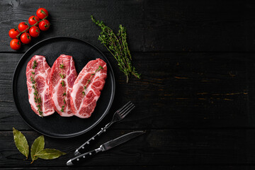Piece of fresh raw pork from the neck, with ingredients, on black wooden table background, top view flat lay, with copy space for text