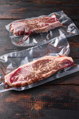 Vacuum packed meat , top blade beef steak on dark old wooden table,  side view selective focus.