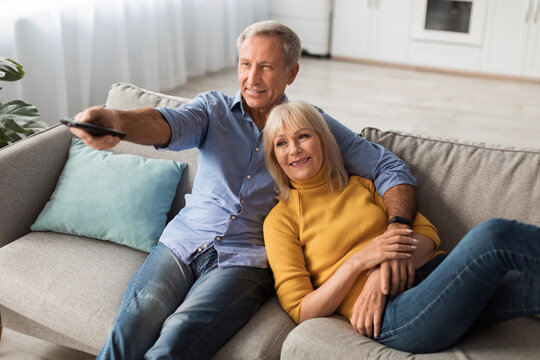Happy Senior Spouses Watching TV Relaxing At Home