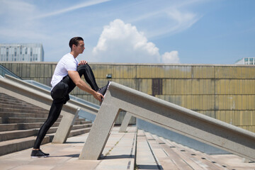 Sporty male is stretching his legs outdoors.