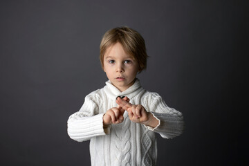 Cute little toddler boy, showing gesture in sign language on gray background, isolated image, child...
