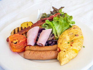 Breakfast set meal, omelette, bacon, ham, sausages, grilled tomato and potato with vegetable salad in hotel for vacation