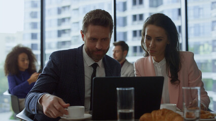 Two professionals discussing business project at laptop online meeting in cafe.