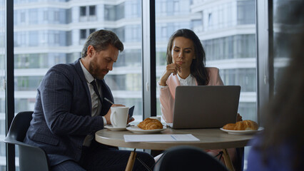 Two coworkers researching laptop computer working online in glass office cafe.