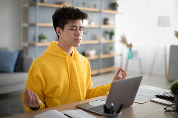 Asian man meditating with closed eyes in front of laptop