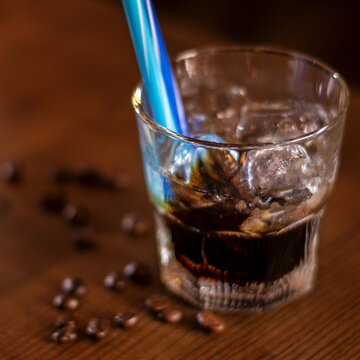 khalua drink with ice in glass with blue straw and coffee beans on wooden table square