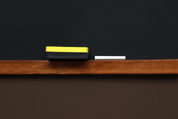 Clean blackboard with chalk and duster hanging on brown wall